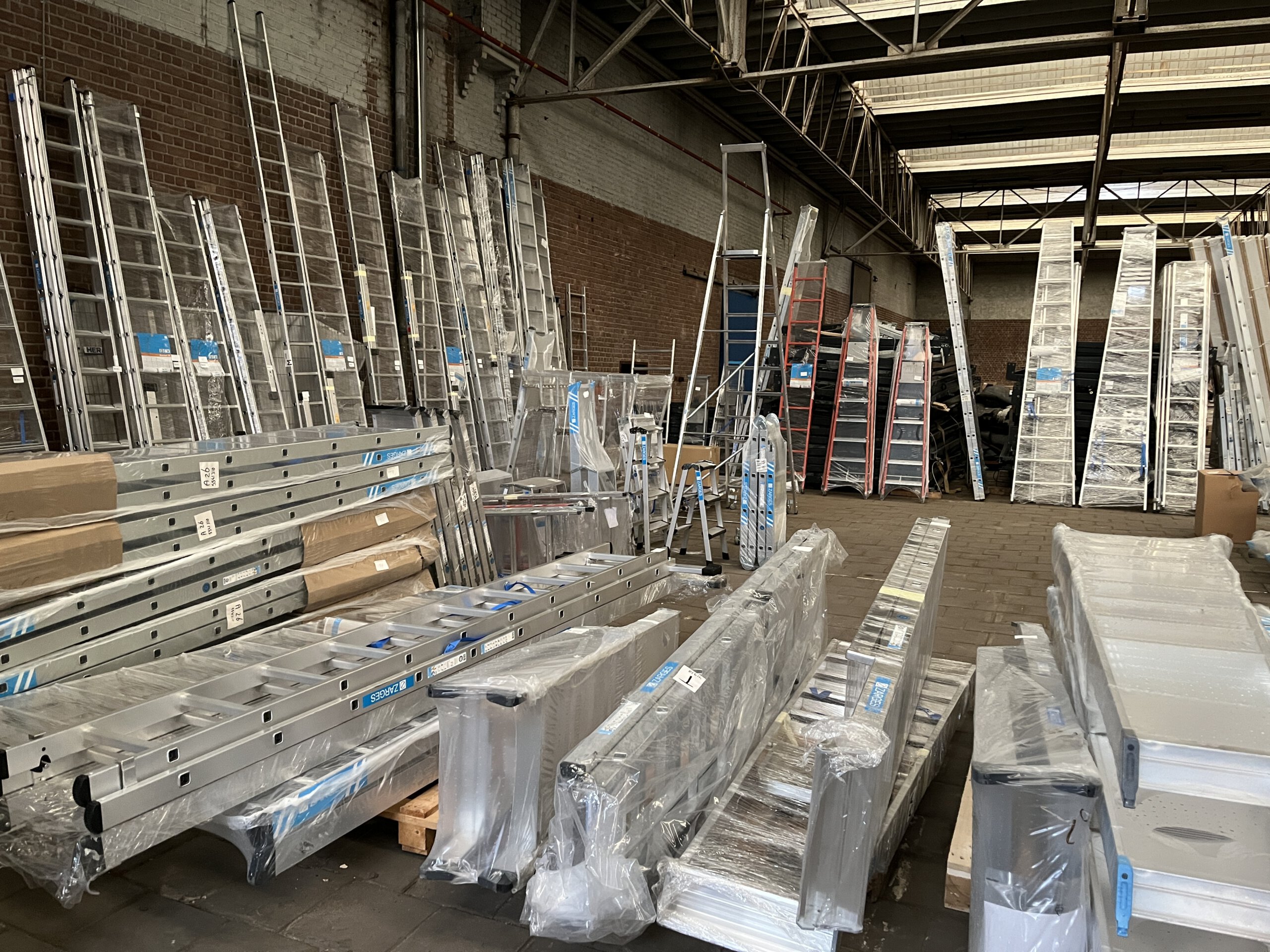 Opkoper van gereedschap met ladders, trappen, steigers en rollend materieel opgeslagen in groot professioneel magazijn voor online veiling