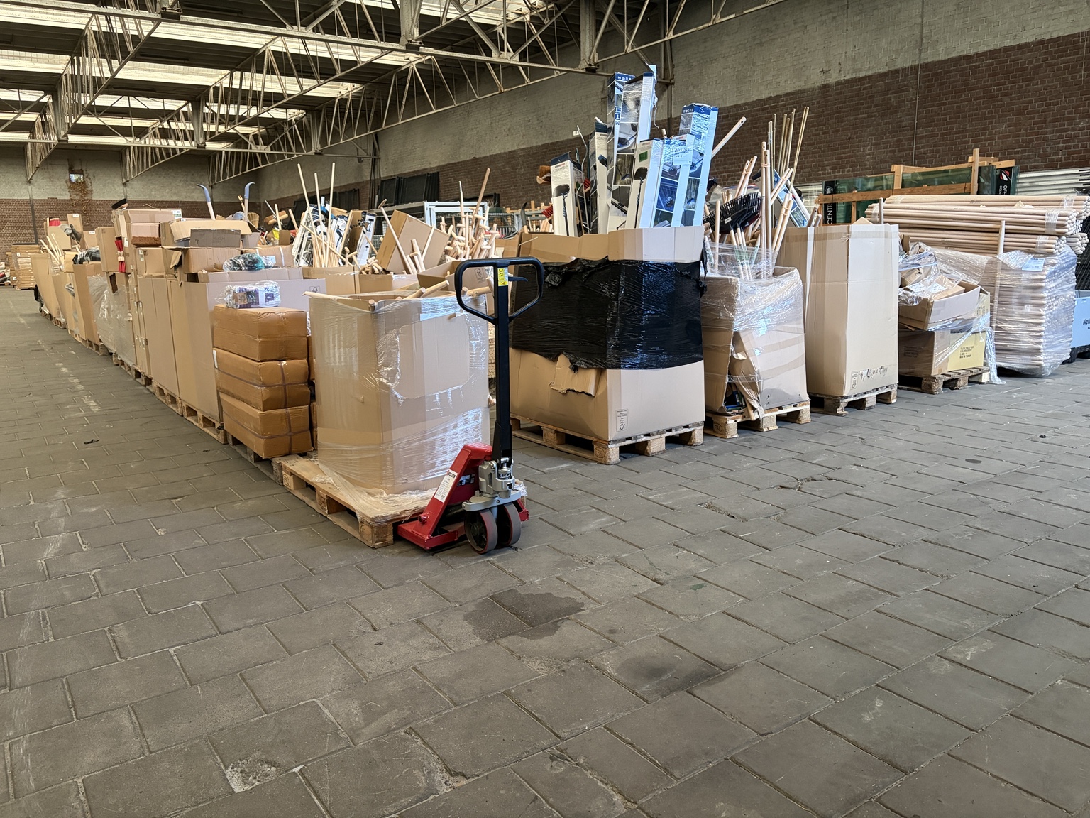 Overzicht van een grote partij bouw- en installatiematerialen op pallets in een bedrijfshal
